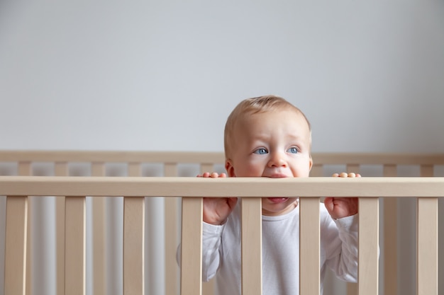 Blond Mignon Petit Bebe Aux Yeux Bleus En Body Blanc Mordant La Tete De Lit En Bois Sur Interieur Blanc Photo Premium