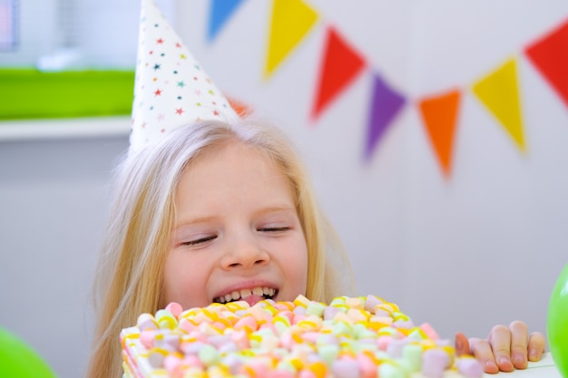 Blonde Fille Caucasienne Furtivement Derriere Le Gateau D Anniversaire Avec Une Drole De Tete Sur La Fete D Anniversaire Fond Colore Festif Avec Des Ballons Photo Premium