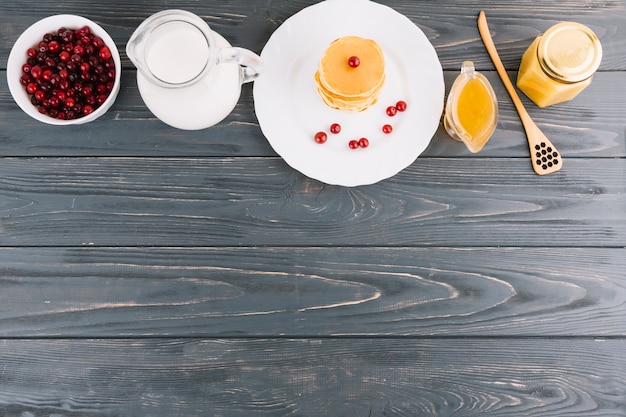 Bol de baies de cassis; lait; miel et crêpes sur un fond texturé en bois Photo gratuit