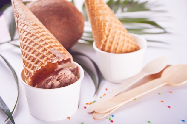 Bols en papier de crème glacée au chocolat avec des cônes de gaufres et des cuillères en bois sur le fond blanc Photo Premium