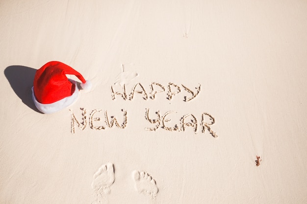 Bonne année écrit dans le sable et santa hat sur la plage de sable blanc Photo Premium