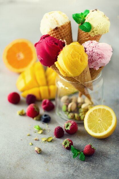 Boules de glace colorées rouges, roses, jaunes, vertes dans des cônes de gaufres aux saveurs différentes - mangue, citron vert, menthe, pistache, orange, fraise, framboise, myrtille. concept d'été Photo Premium