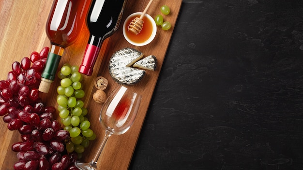 Bouteilles de vin rouges et blancs avec grappe de raisin, fromage, miel, noix et verre à vin sur bois Photo Premium