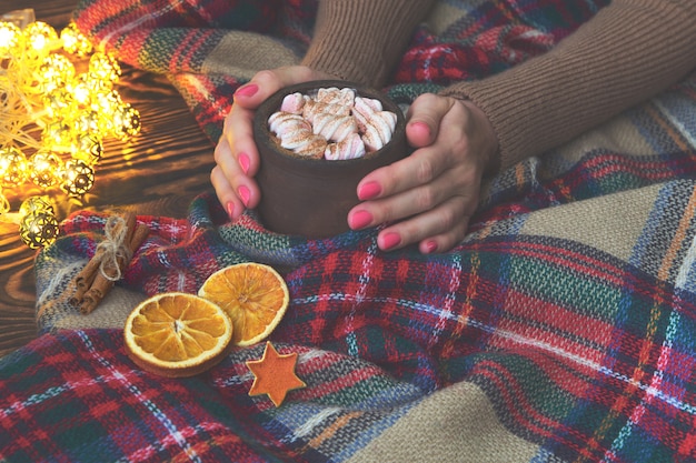 Cacao chaud avec guimauve à la main fille en pull, couverture et oranges sèches avec des lumières de noël. noël, hiver, notion de nouvel an. espace de copie, Photo Premium