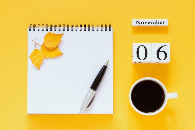 Calendrier 6 novembre tasse de café, bloc-notes avec stylo et feuille jaune sur une surface jaune Photo Premium