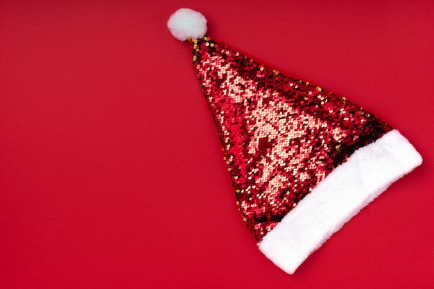 Chapeau de père noël mousseux de noël sur fond rouge. fond de vacances de noël noël nouvel an. accessoire de nouvel an. carte de voeux joyeux noël. vue de dessus, pose à plat, espace de copie Photo Premium