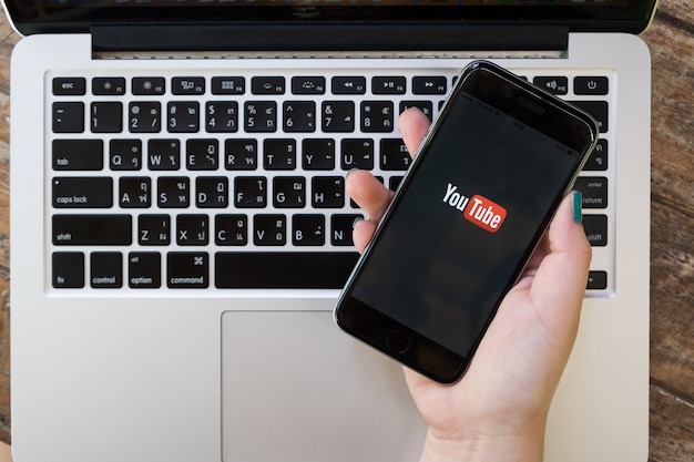 Chiang mai, thaïlande - 1er octobre 2017: une femme montrant une capture d'écran de youtube sur un iphone 6s. application youtube à l'écran, allongée sur un vieux bureau en bois. youtube est le site web de partage de vidéos en ligne populaire. Photo Premium