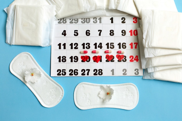 Concept de cycle de menstruation. calendrier des menstruations avec serviettes hygiéniques, pilules contraceptives et fleurs. Photo Premium