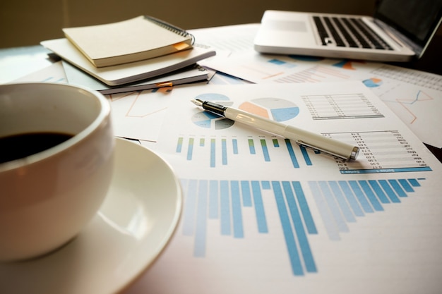 Concept d'entreprise avec espace de copie. table de bureau avec stylo et tableau d'analyse, ordinateur, ordinateur portable, tasse de café sur le bureau. tonalité de rétro filtre rétro, mise au point sélective. Photo gratuit