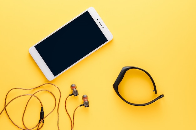 Concept de remise en forme avec téléphone portable, écouteurs et tracker de remise en forme sur fond jaune Photo Premium