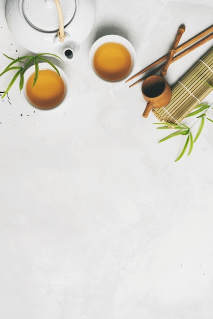 Concept de thé asiatique, deux tasses blanches de thé, théière, service à thé, baguettes, tapis de bambou entourés de thé vert sec sur fond blanc avec espace de copie. infuser et boire du thé. Photo Premium