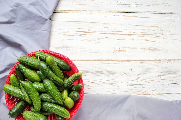 Concombres organiques fraîches dans un panier rouge sur une table en bois blanche avec poivrons verts et rouges, piment, fenouil, sel, poivre noir, ail, pois, gros plan, concept santé, vue de dessus, pose à plat Photo gratuit