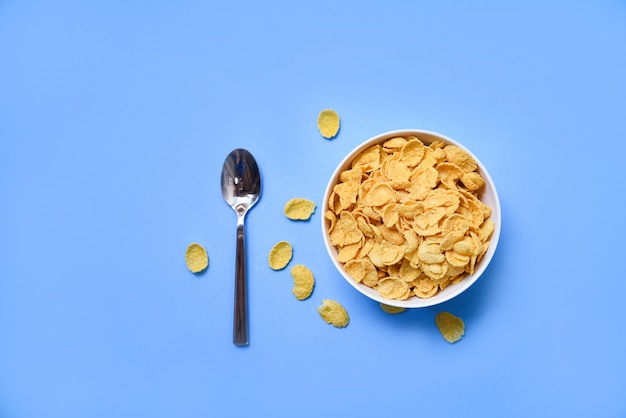 Cornflakes dans un bol sur bleu et une cuillère pour des aliments sains de céréales Photo Premium