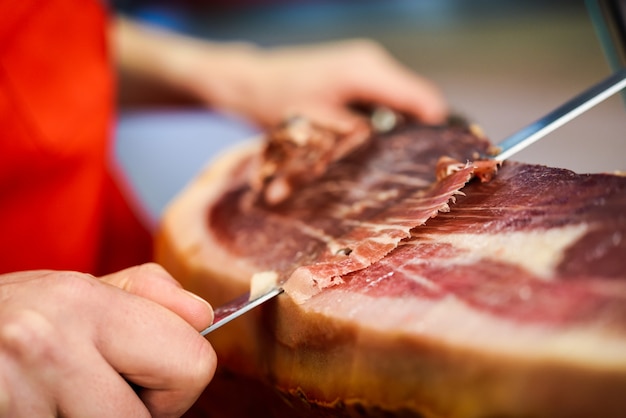 Coupe professionnelle découpant des tranches d'un jambon serrano avec os complet Photo gratuit
