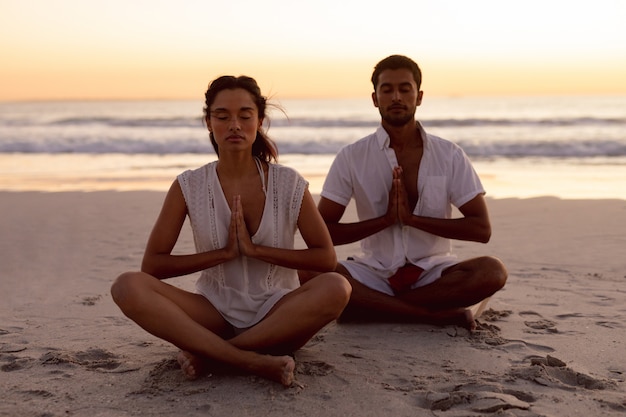 Couple effectuant le yoga ensemble sur la plage Photo gratuit