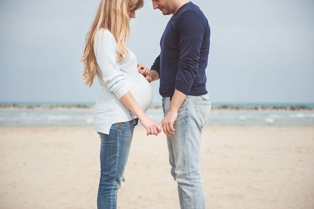 Couple enceinte sur la plage. les mains sur le ventre. Photo Premium