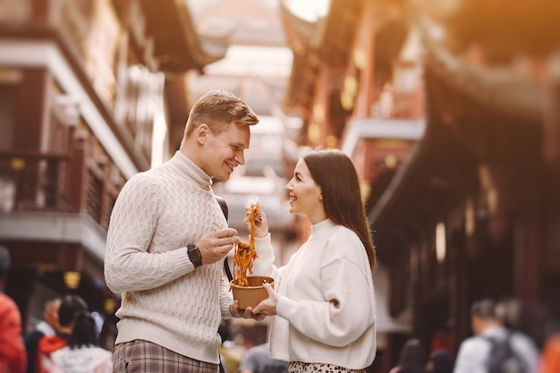 Couple De Jeunes Mariés Manger Des Nouilles Avec Des Baguettes à Shanghai à L'extérieur D'un Marché Alimentaire Photo gratuit