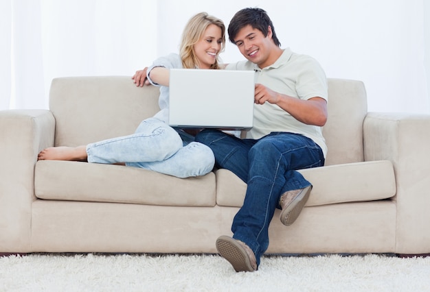 Un Couple Souriant Sont Assis Sur Un Canapé En Regardant Un Ordinateur Portable Photo Premium 