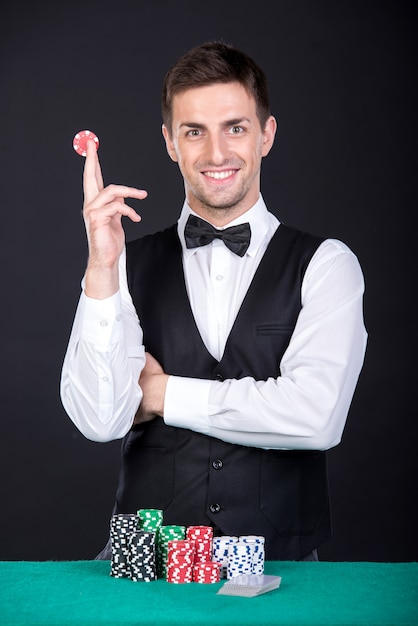 Croupier souriant avec des jetons de jeu sur la table verte. Photo Premium
