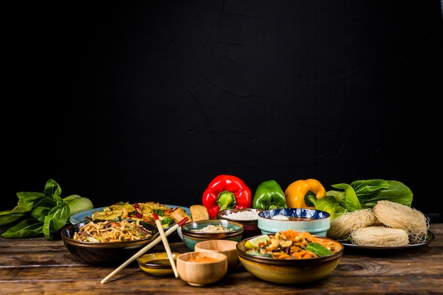 Délicieuse variété de plats thaïlandais dans différents bols avec bokchoy et poivrons sur une table sur fond noir Photo gratuit