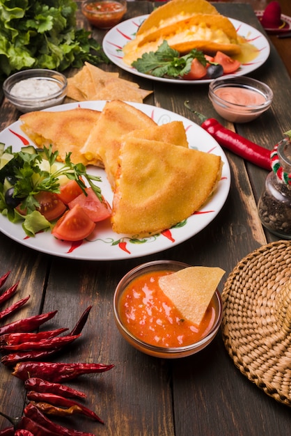 De délicieux gâteaux près de salades de légumes sur des assiettes parmi des nachos avec des sauces Photo gratuit