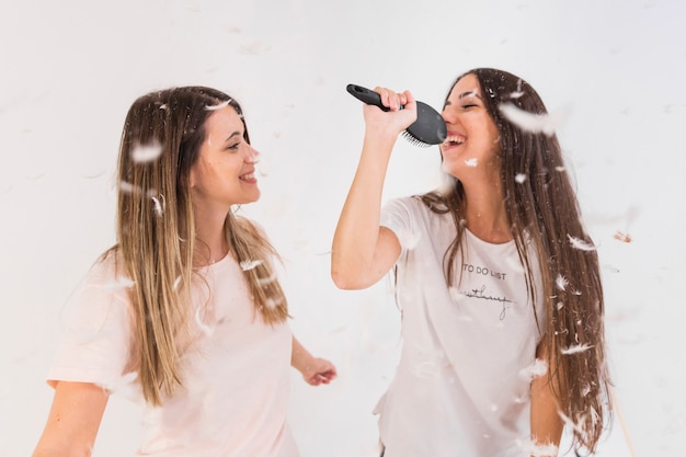 Deux amies chantent des chansons et s'amusent avec des plumes dans l'air Photo gratuit