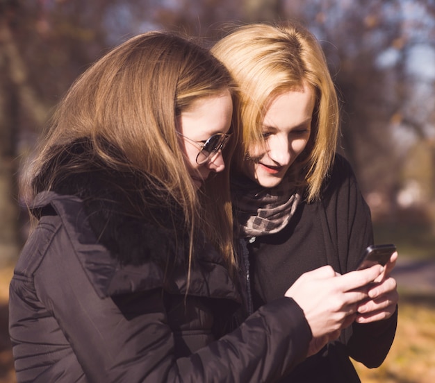 Deux amis femmes heureux partageant les médias sociaux dans un téléphone intelligent à l'extérieur dans un parc Photo Premium