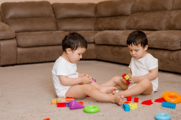 Deux Bebes Garcons Jumeaux Sont Assis Sur Le Sol De La Maison Et Jouent A Des Jeux Educatifs Enfant Jouant Avec Des Jouets Colores Photo Premium