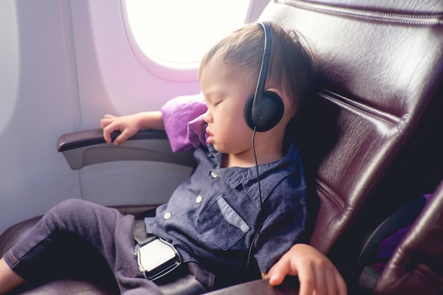 Enfant De Bebe Garcon Bebe Dort Avec La Ceinture De Securite Sur Portant Des Ecouteurs Lors D Un Voyage En Avion Photo Premium