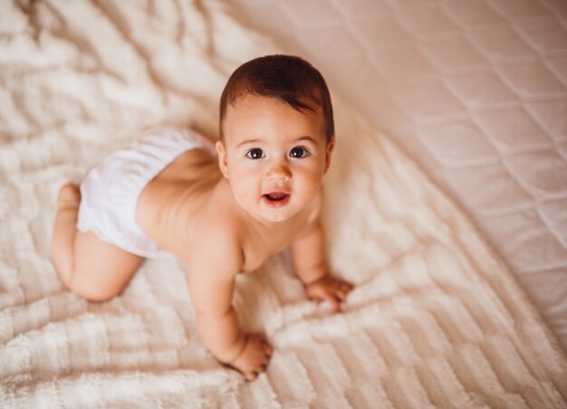 Enfant dans une couche se trouve sur le lit recouvert d'une couverture blanche douce Photo Premium