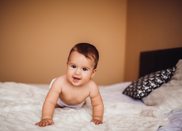 Enfant dans une couche se trouve sur le lit recouvert d'une couverture blanche douce Photo Premium