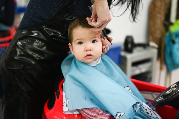 L Enfant Se Fait Couper Les Cheveux Chez Le Coiffeur Dans Une Voiture Rouge La Premiere Coupe De Cheveux De L Enfant Chez Le Coiffeur Enfant En Bas Age Se Coupe Les Cheveux