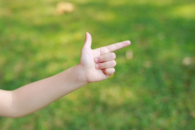Enfants main pointant avec l'index ou en faisant un geste de pistolet sur flou jardin vert. la main de l'enfant montre l'index correct ou le point. Photo Premium