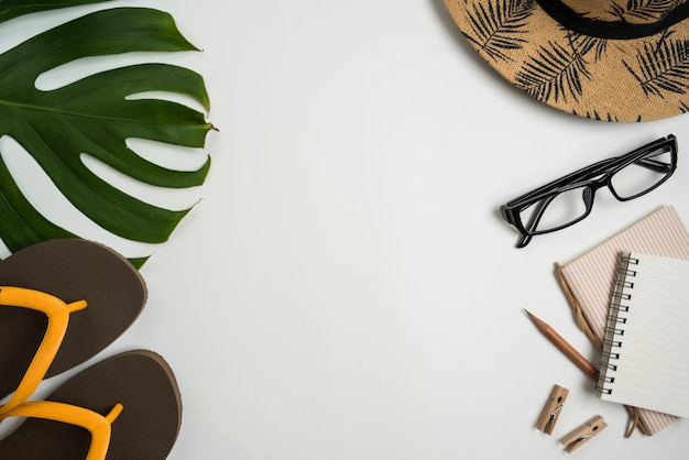 Espace de travail vue de dessus plat avec lunettes, cahier, chapeau, crayon, feuille verte, chaussures et tasse à café sur fond blanc. Photo Premium