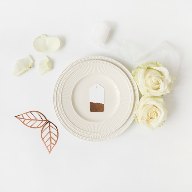 Étiquette vierge sur plaque blanche avec rose; feuilles et ruban sur fond blanc Photo gratuit