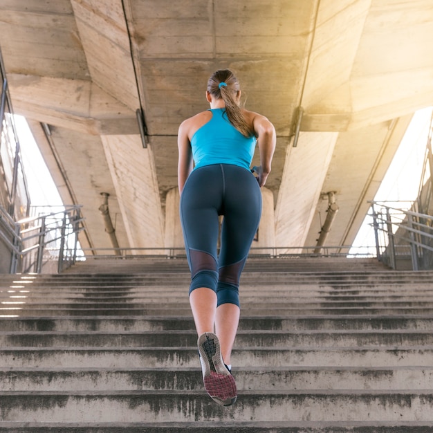Faible angle de vue de jogger féminin en cours d'exécution sur l'escalier sous le pont Photo gratuit