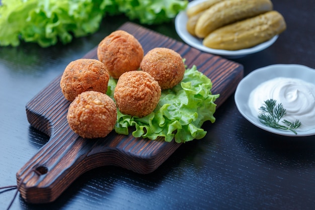 Falafel repose sur une planche à découper en bois. sur la table, tomates, concombres, laitue, aneth, citron, crème sure. plat national du moyen-orient. Photo Premium