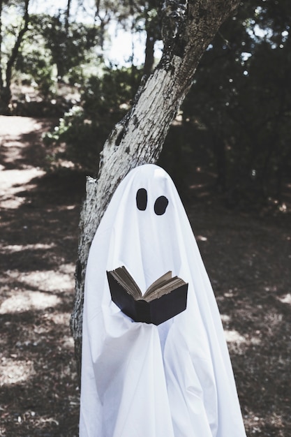 Fantôme debout à l'arbre et livre de lecture Photo gratuit