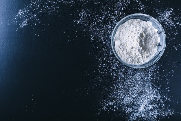 Farine blanche saupoudrée sur une table en bois sombre. vue de dessus Photo Premium