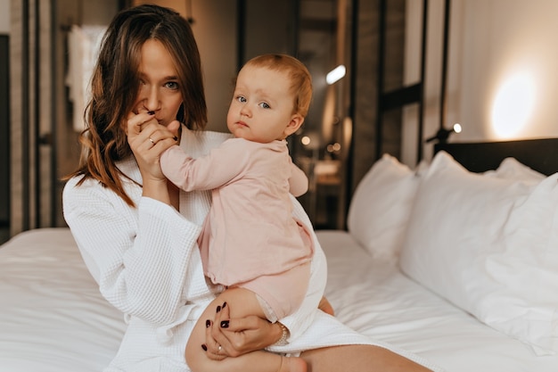 Femme Aux Yeux Verts En Peignoir Baise La Main De Son Enfant Maman Et Fille Posent A La Maison Assis Sur Le Lit Photo Gratuite