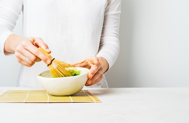Femme en blanc prépare le thé vert japonais matcha en le fouettant dans un bol Photo Premium