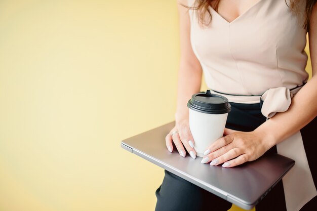 Une femme brune aux cheveux bouclés rigole devant un ordinateur portable dans un étui jaune. il y a un smartphone sur un chargeur jaune sur la table. Photo Premium