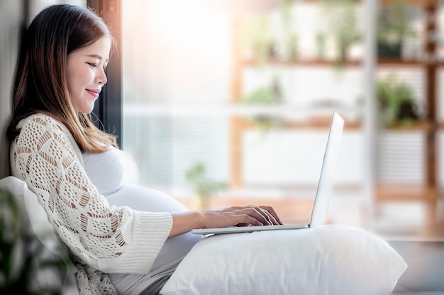 Femme enceinte à l'aide d'un ordinateur portable à la maison. Photo Premium