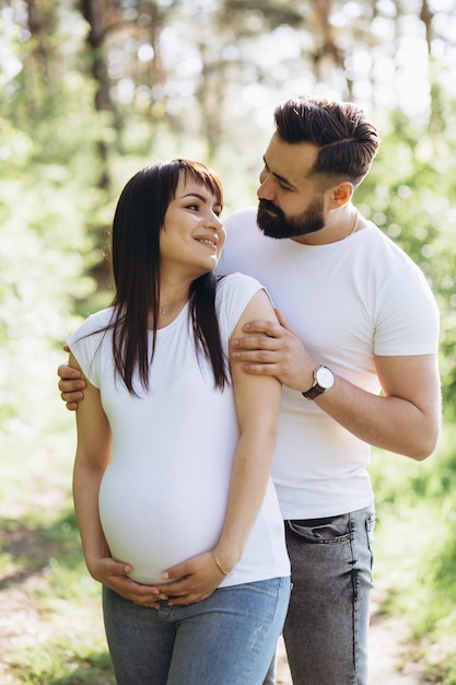 Femme enceinte et son mari aux cheveux étreignant sur le ventre ensemble dans la nature en plein air Photo Premium