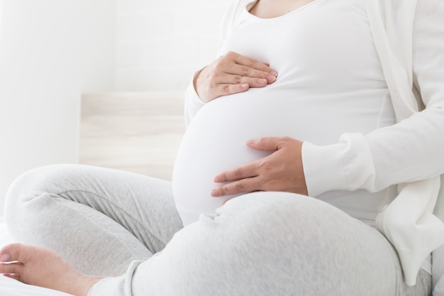 Une Femme Enceinte Tient Ses Mains Sur Son Ventre Gonfle Sur Un Lit Blanc Aime Et Se Sent Joyeuse Comme Affectif Affecte Le Developpement Neurologique Et Psychologique De Bebe Photo Premium