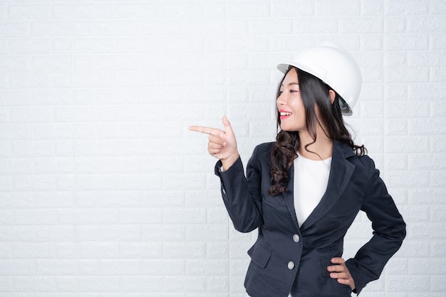 Femme d'ingénierie tenant un chapeau, séparer le mur de briques blanches fait des gestes avec la langue des signes. Photo gratuit