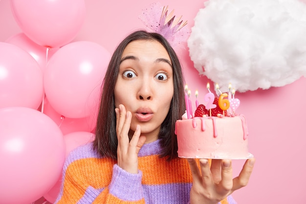 La Femme Regarde Se Demande A L Appareil Photo Tient Un Delicieux Gateau D Anniversaire Savoureux Porte Une Couronne Et Des Poses De Cavalier Raye Photo Gratuite