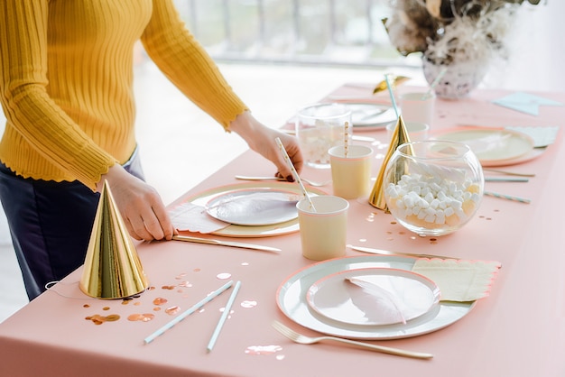 Femme Servant Une Table De Fete Dans Des Couleurs Pastel Avec Une Nappe Rose Des Plats En Papier Colores Des Tasses Et Des Couverts Dores Joyeux Anniversaire Pour Fille Photo Premium