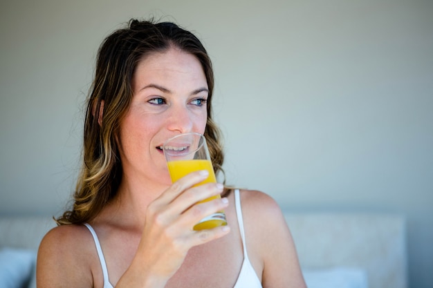 Femme souriante, sirotant un verre de jus d'orange dans sa ...