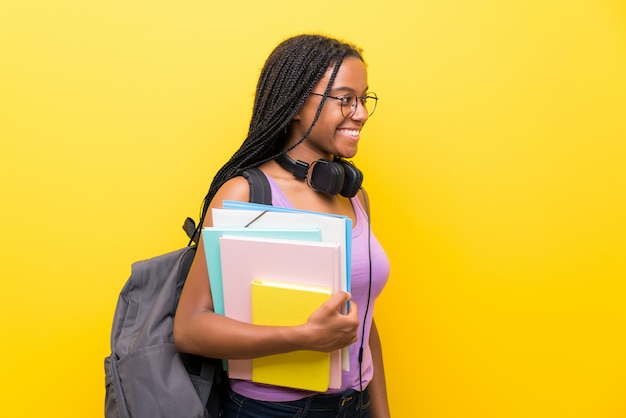 Fille étudiante adolescente afro-américaine avec de longs cheveux tressés sur un mur jaune isolé à la recherche du côté Photo Premium